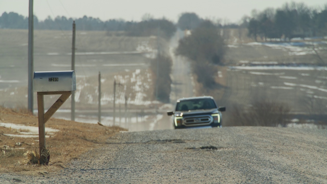 一辆皮卡在乡村的砾石农场道路上向一个邮箱驶去。视频下载