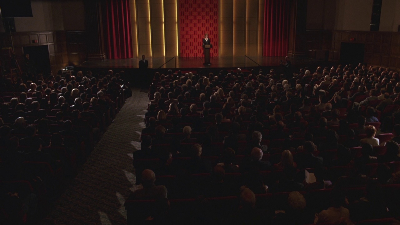 拥挤的剧院或礼堂的广角。观众或人群坐着，而一个女人站在讲台上。镜头是从剧院的后面，观众的后面拍摄的。观众起立，鼓掌，鼓掌。视频素材