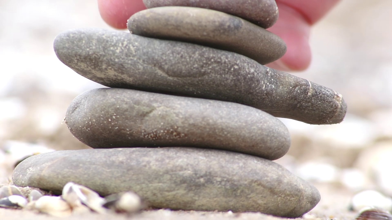 欧洲男性手工堆砌的石堆在宁静的河岸，手指与鹅卵石平静的运动，表现出自然中禅意般的和谐与放松，海岸边的石头金字塔视频素材