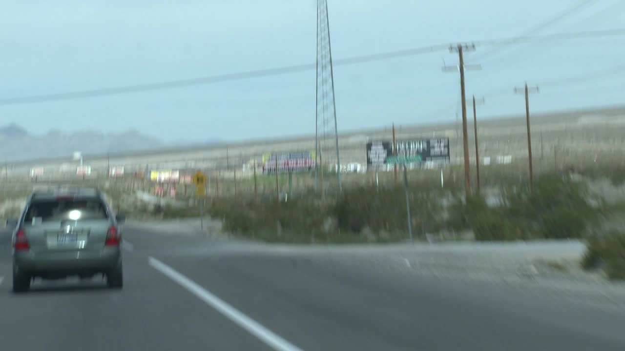 在内华达州靠近拉斯维加斯的沙漠公路上，手持驾驶pov。沙漠景观与郊区和住宅开发前的山脉在bg。路边有各种各样的广告牌和标志。视频下载