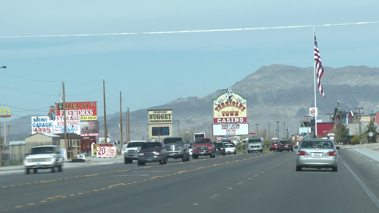 手持驾驶pov在沙漠小镇帕伦普内华达的主要街道。内华达州拉斯维加斯附近的沙漠公路。景观与郊区和住宅开发前的山脉在bg。各种各样的广告牌和标志，路边，连同美国视频下载