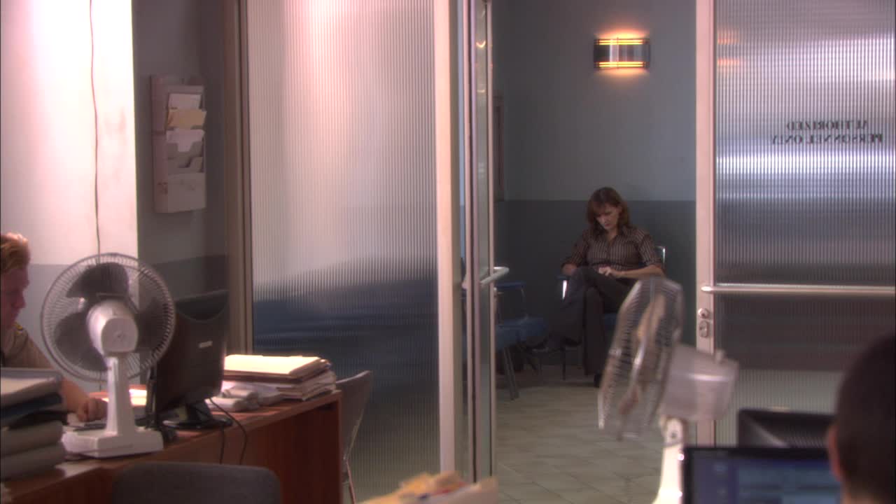警察局的中等角度。带电脑的办公桌支持文书工作和fg的人员。女士们坐在候诊室外的椅子上。穿制服的警官从右向左穿过办公室。视频下载