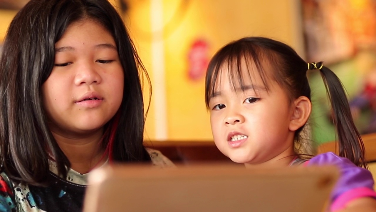 两个小女孩(7岁和11岁)一起玩平板电脑视频素材