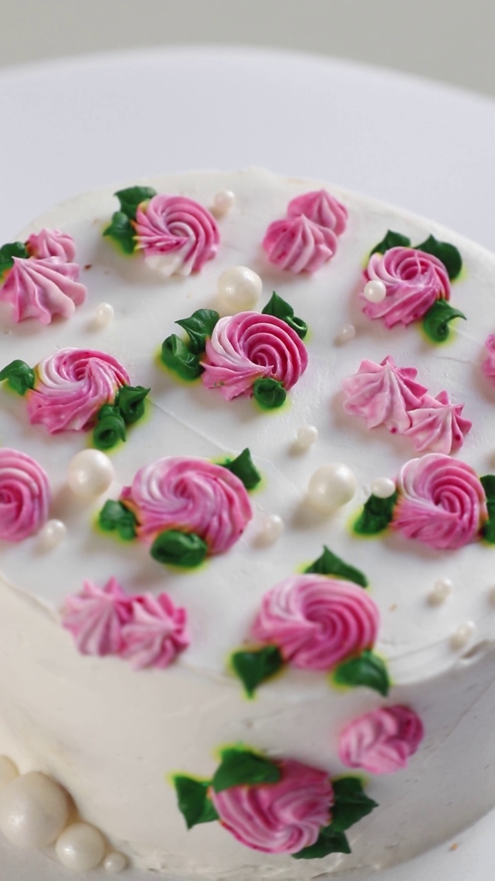 圆形蛋糕与白色奶油和粉红色玫瑰旋转，侧视图。垂直镜头视频下载