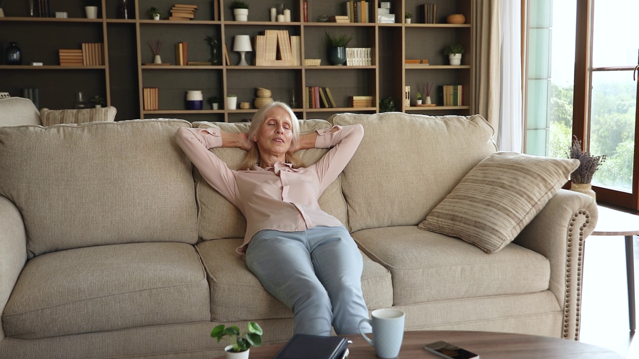 快乐的退休女性享受和平的时刻，放松在舒适的沙发上视频素材