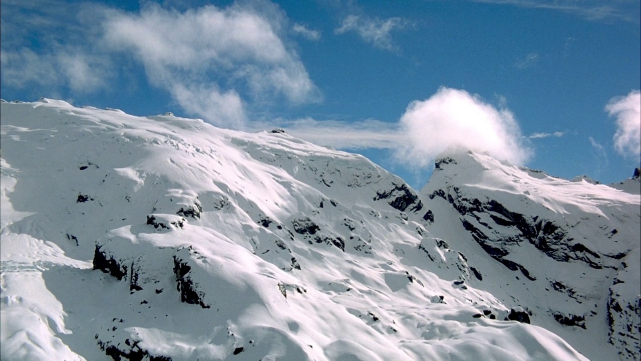 在绿意盎然的群山上空飞越云层。看到白雪皑皑的山峰在云海之上升起。看pov飞在雪山的山峰。在背景中可以看到蓝天和卷云。视频素材