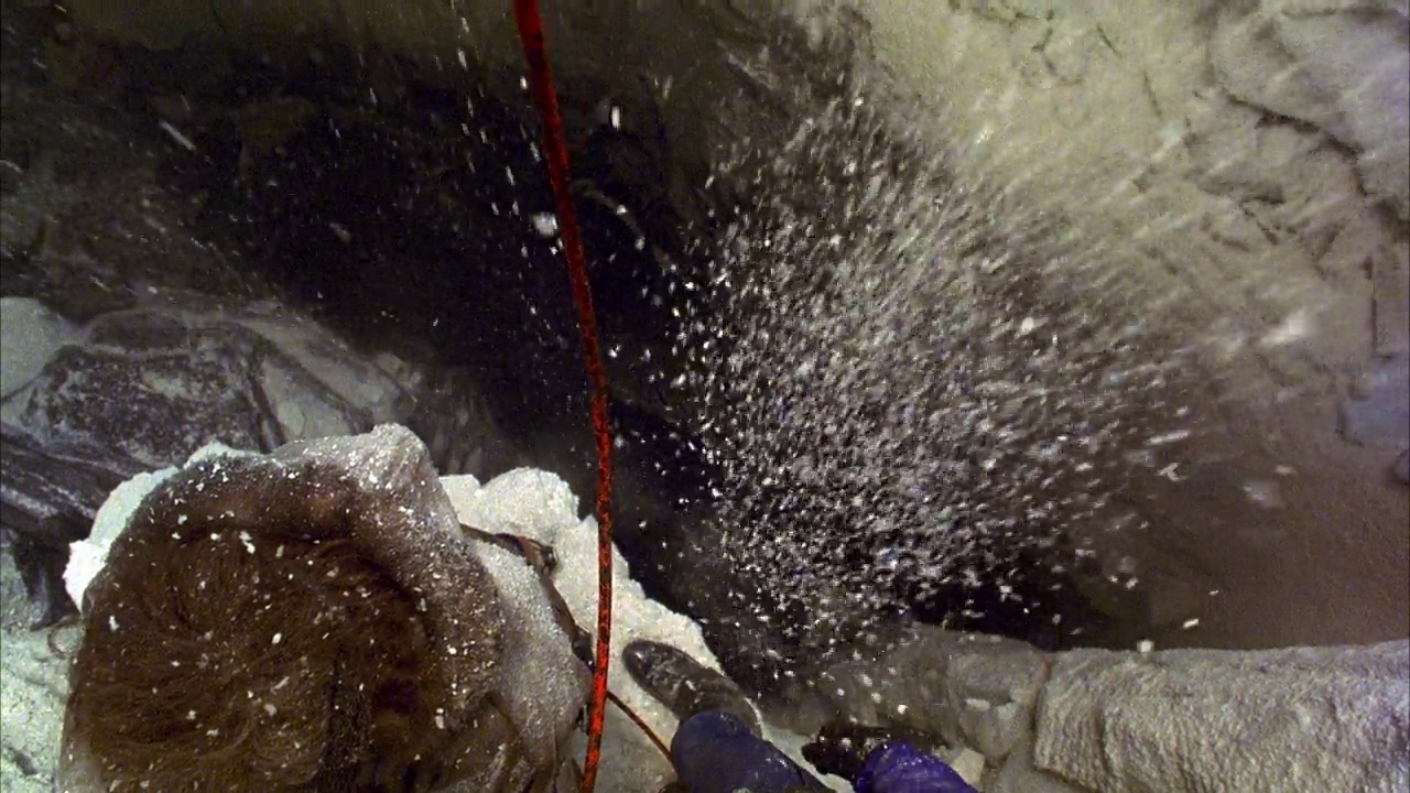 在冰洞或雪洞的深裂缝的高角度下。左下角看到登山者站在岩架上。见红绳垂直横架。看到雪和大块的冰块从pov上脱落，蓝衣攀援者向后跌入裂缝，拉着SEC视频素材