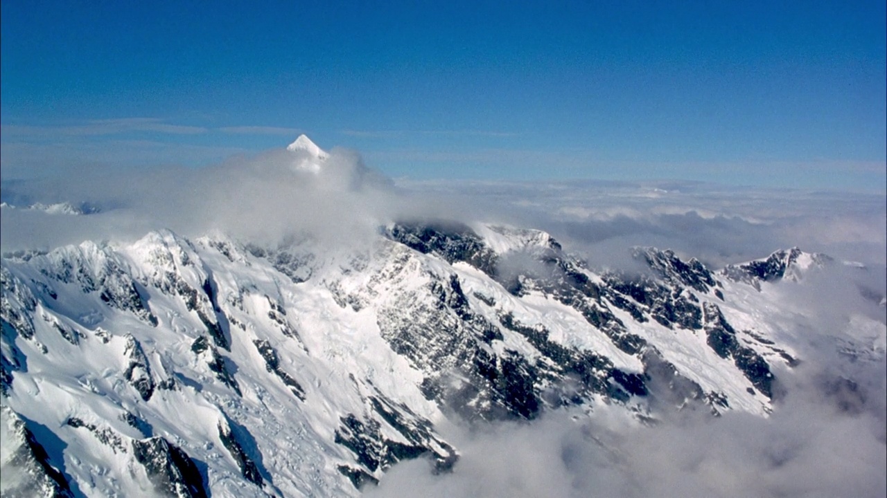 在白雪皑皑的山脉上空飞行。看白云在山峰上翻滚。看到pov沿着山脉的一侧穿过云层，越过尖锐的山峰，向部分被云层遮挡的最高的山峰飞去。看云海和一些低低的豌豆视频素材