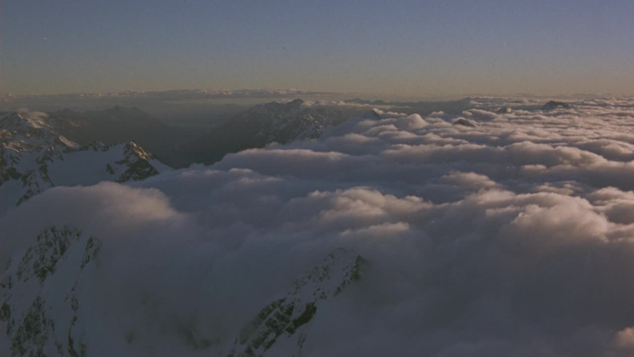 白色积云的空中覆盖物。看雪山。看到山顶与白色积云毯子在底部和周围的山脉。看波峰从云天的一边飘到另一边。用光晕和透镜光圈看太阳视频素材