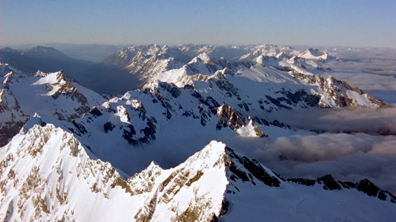 白雪皑皑的山脉。看到山顶与白色积云毯子在底部和周围的山脉。看波峰从云天的一边飘到另一边。视频下载