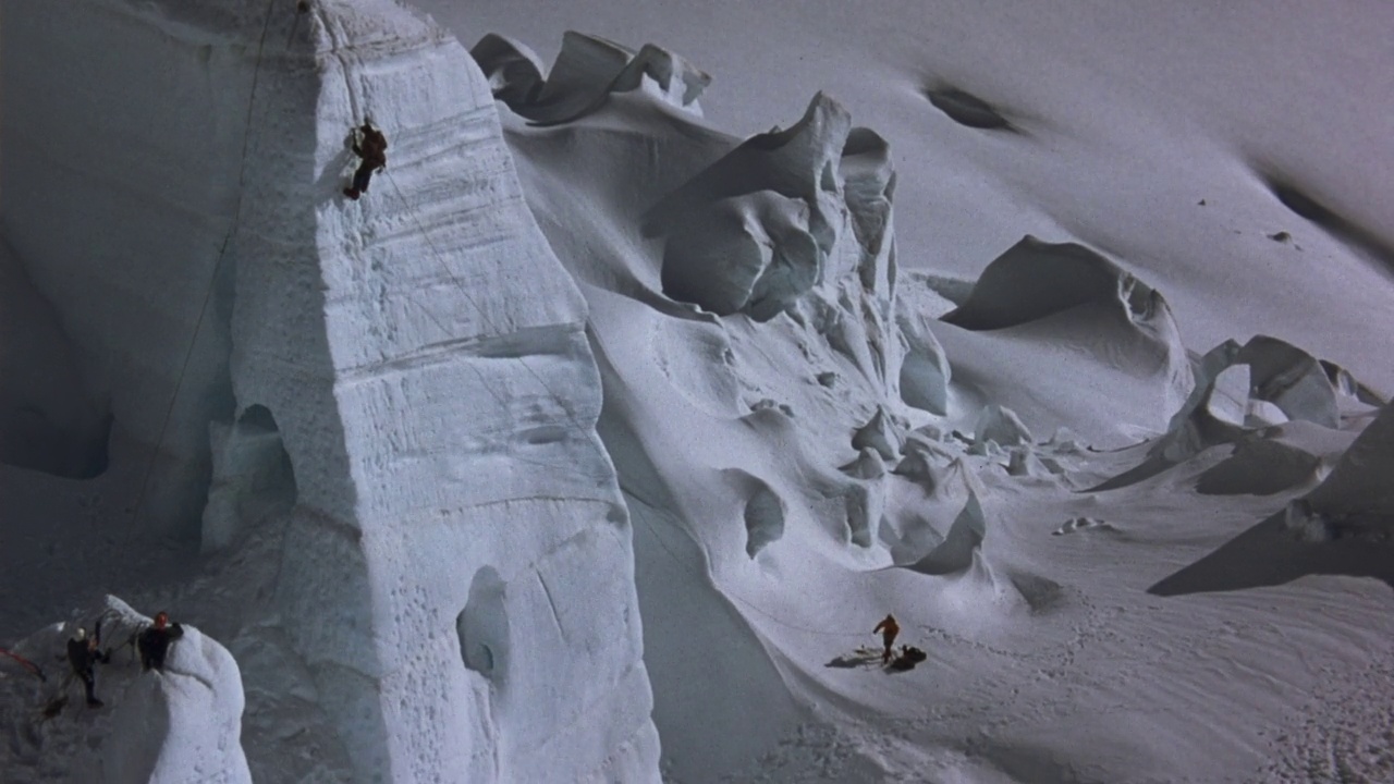 登山者在陡峭的白色冰或雪悬崖或墙壁上的空中拍摄。用镐和雪鞋在登山时向后拉。向后拉，看用绳索系在攀登者身上的墙的左右两侧的侦察员。视频素材