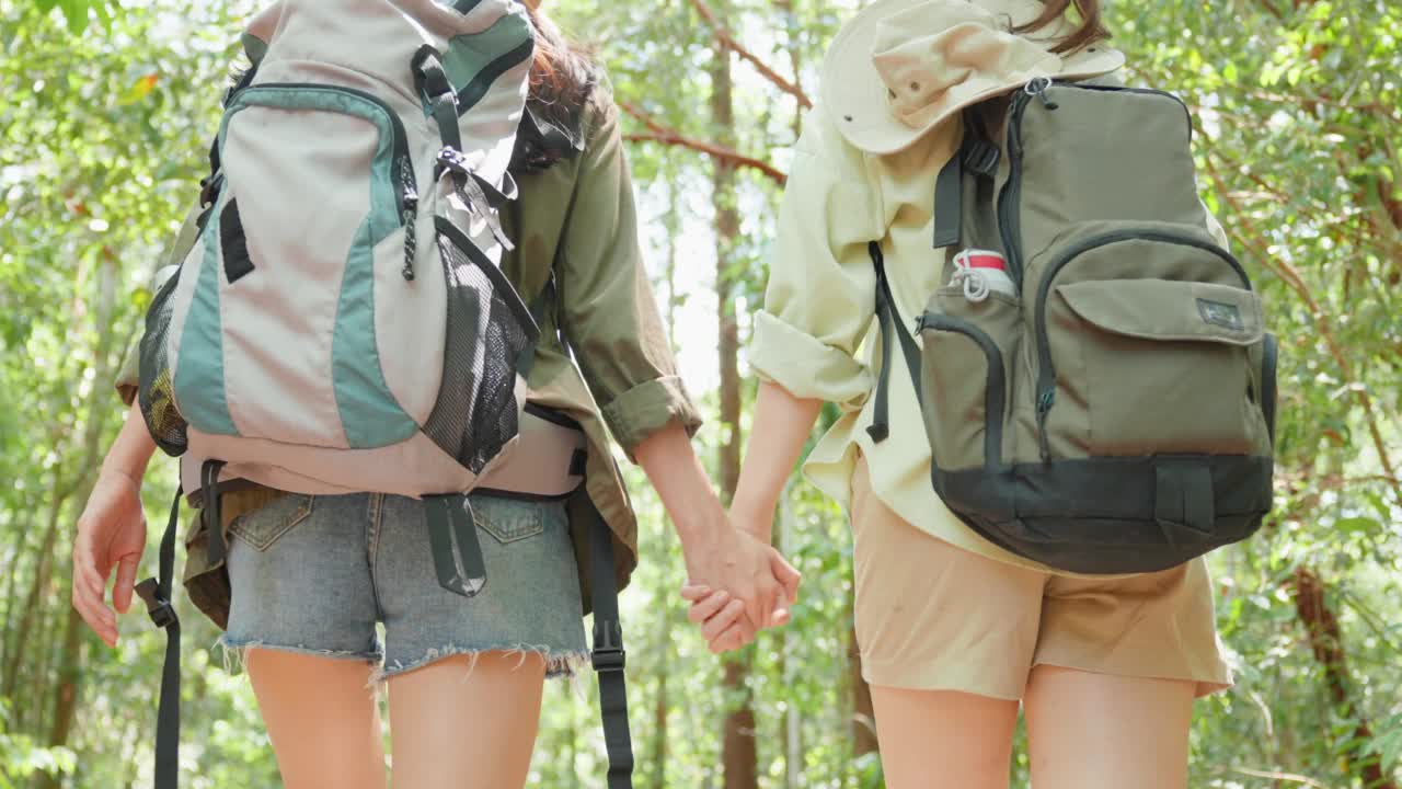 亚洲美丽的两个女人背包旅行在森林野生一起。迷人的年轻女性朋友们在夏天的假期旅行期间散步和探索自然树林的快乐。视频下载