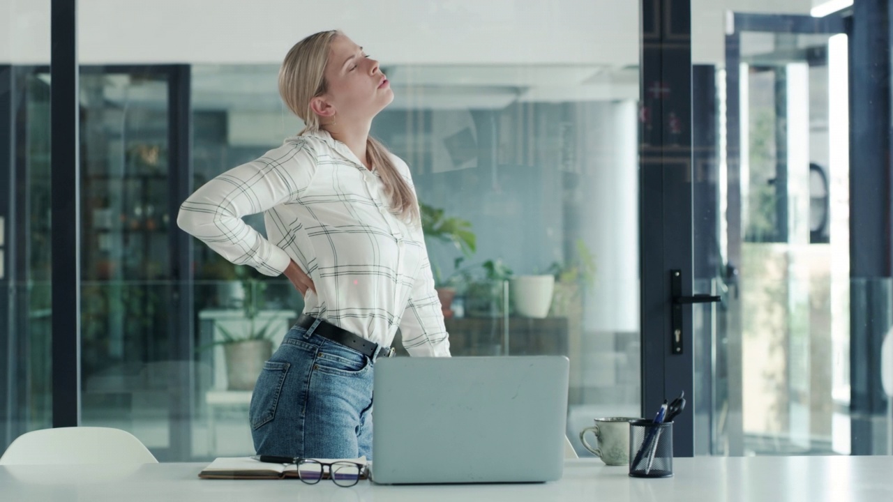 一位年轻的女商人在现代办公室的办公桌前工作时背部疼痛。女商人看起来工作压力很大视频素材