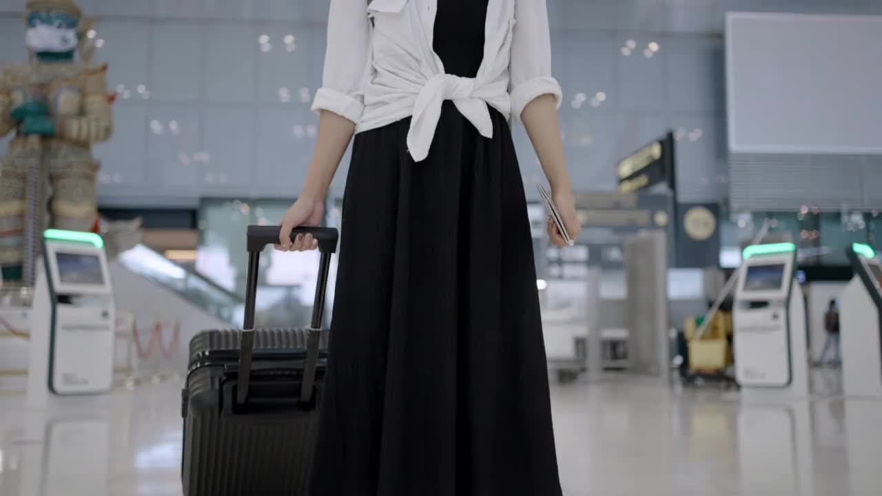 一名亚洲年轻女子戴着防护口罩，拿着行李在机场候机楼走着视频素材