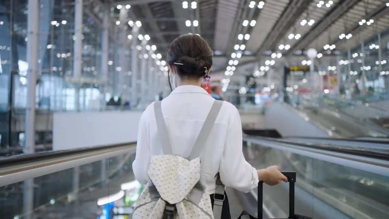 亚洲年轻女商人戴着口罩站在机场候机楼的自动扶梯上视频素材