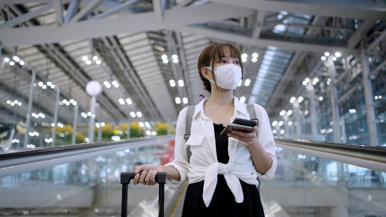 亚洲年轻女商人戴着口罩，在机场候机楼的自动扶梯上打电话视频素材