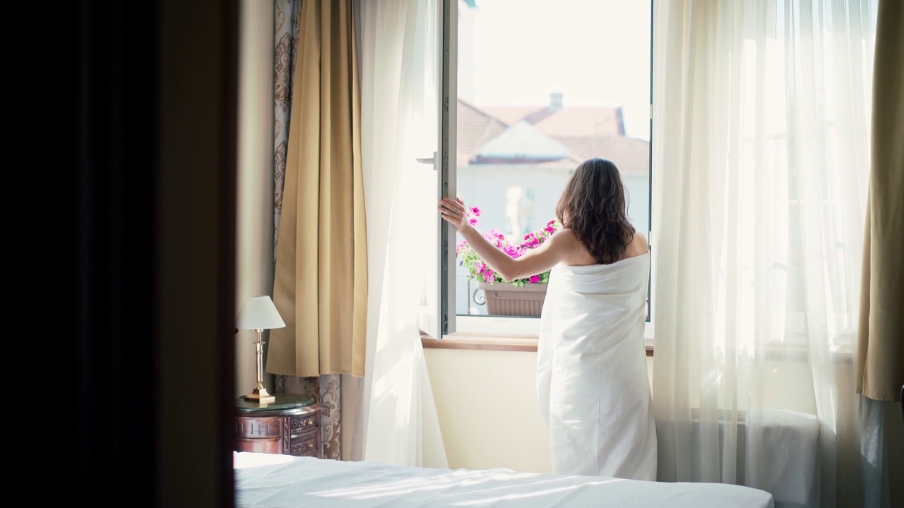 一个裹着毯子的年轻女子打开了酒店房间的窗帘视频素材