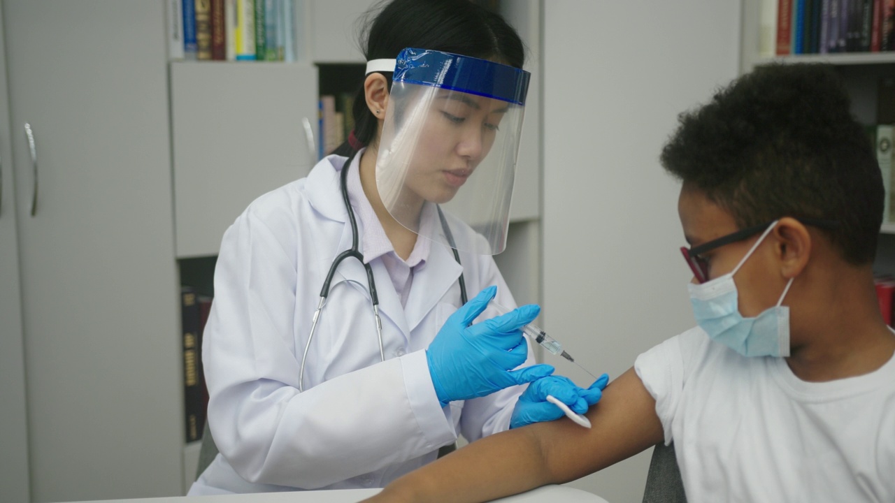 亚洲护士为戴眼镜和口罩的拉丁男孩制造疫苗视频素材