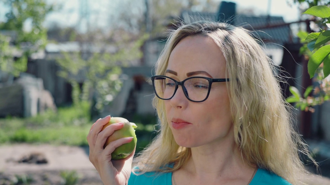 一个年轻女人咬着吃着一个成熟的红苹果，看着花园里的摄像机，慢动作。健康饮食和美容。饮食。视频素材