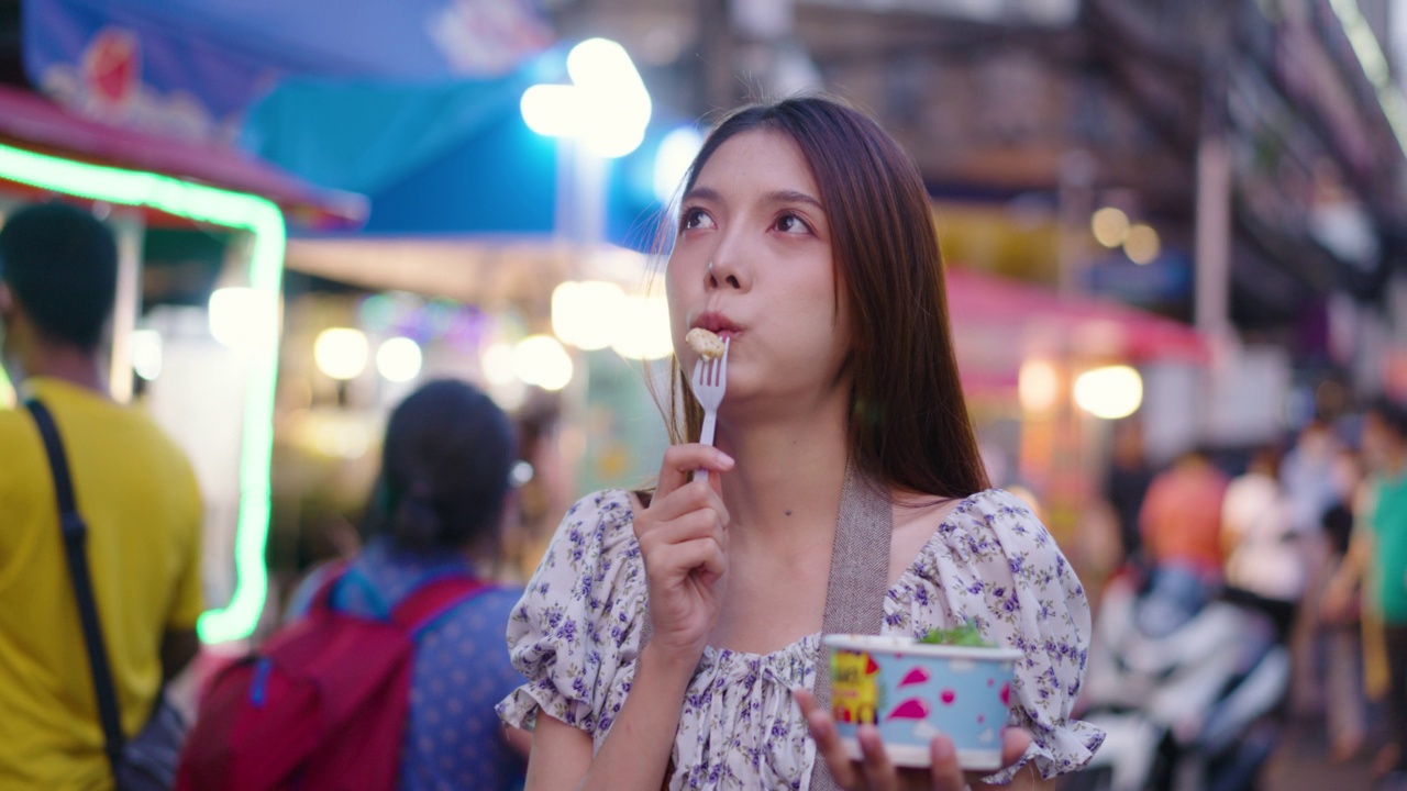 女游客在街头小吃街吃冰淇淋。视频素材