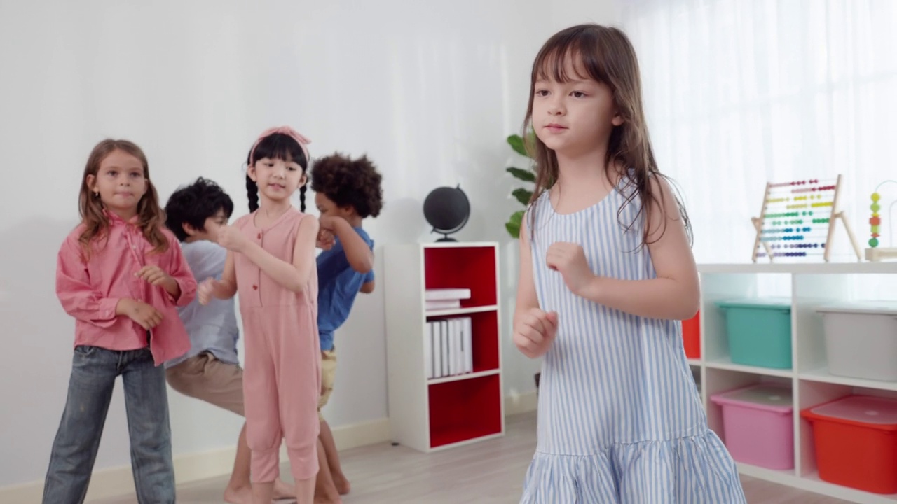 可爱的亚洲6岁女学生身穿蓝色条纹裙，在她的朋友面前跳舞，两个可爱的小男孩拉着他们的手，欢快地跳着。视频素材