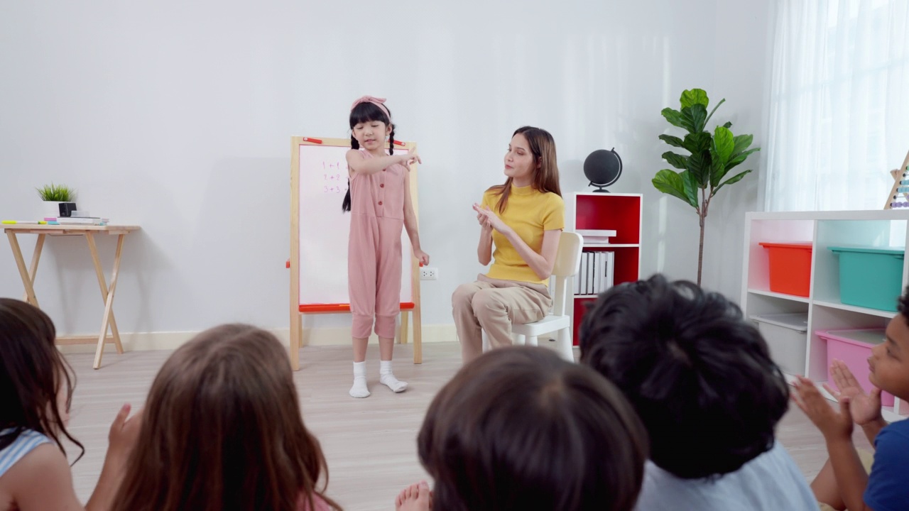 可爱的亚洲女生戴着粉红色的蝴蝶结，穿着休闲的衣服，在老师和朋友们的掌声和歌声中翩翩起舞。视频素材