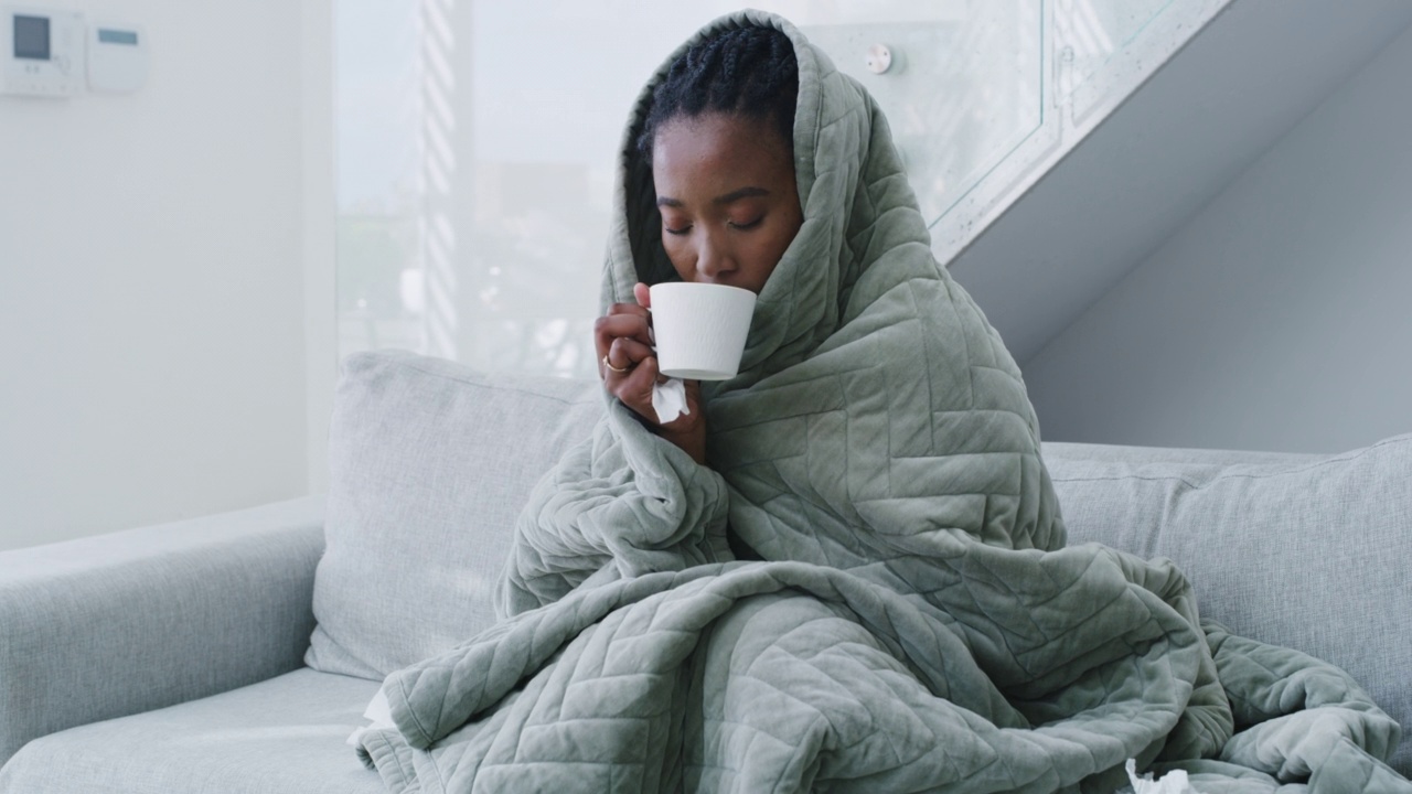 一位年轻女子因感冒卧床在家。女人感觉不舒服，盖着毯子喝茶视频下载