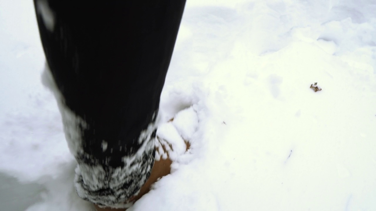 一个穿着棕色靴子的男人在霜冻的冬天走在大雪堆上视频下载