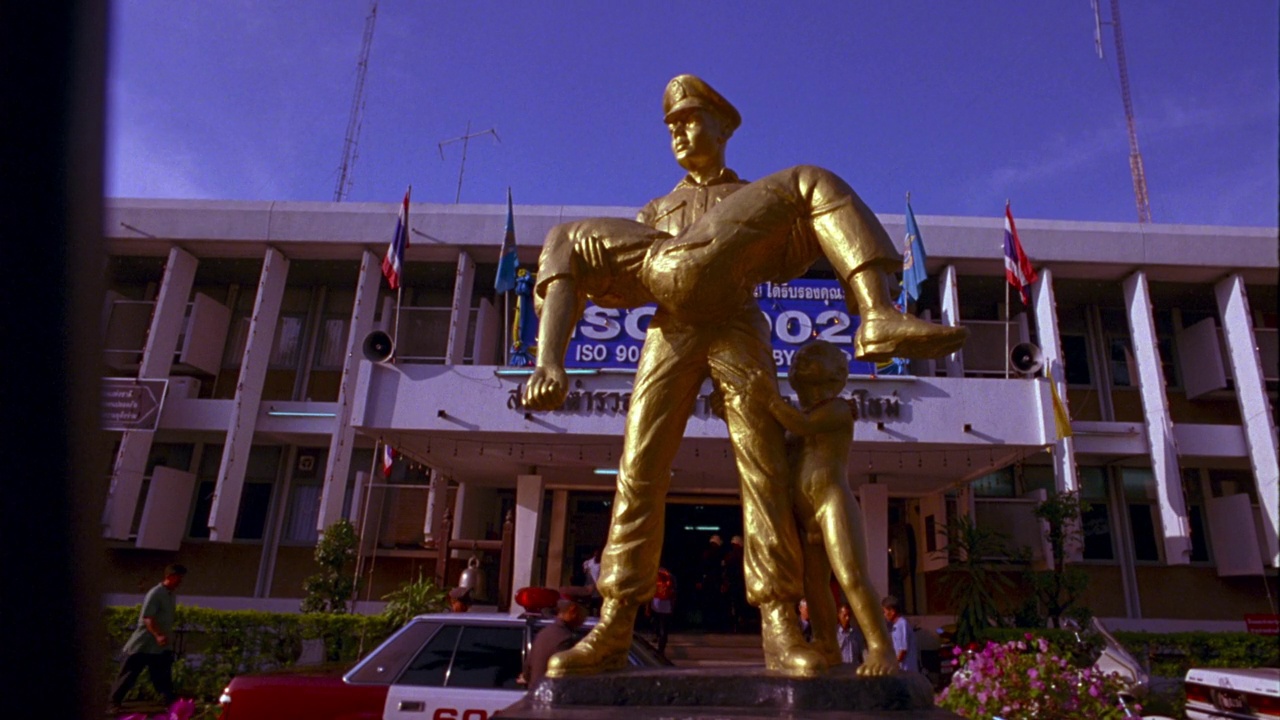 中等角度的黄金雕像的警察或警察抱着一个男孩在他的手臂在泰国或亚洲。镜头从雕像上移开，然后回到雕像上。在后台看到警察局或总部。看到警车停在大楼前。人走在视频素材