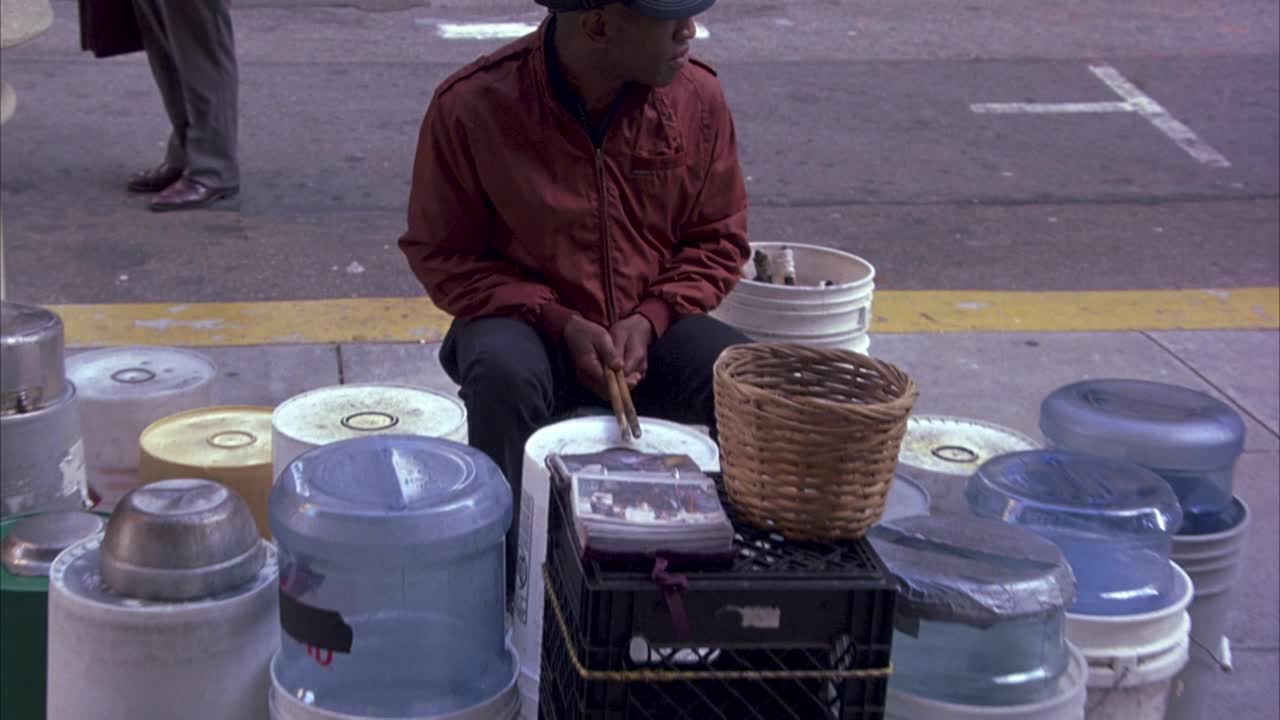 街头艺人手持唱歌和演奏的临时架子鼓，由盒子、油漆容器、牛奶箱、金属罐和饮水机瓶制成。路人把钱放在篮子里。男人,音乐家。视频下载