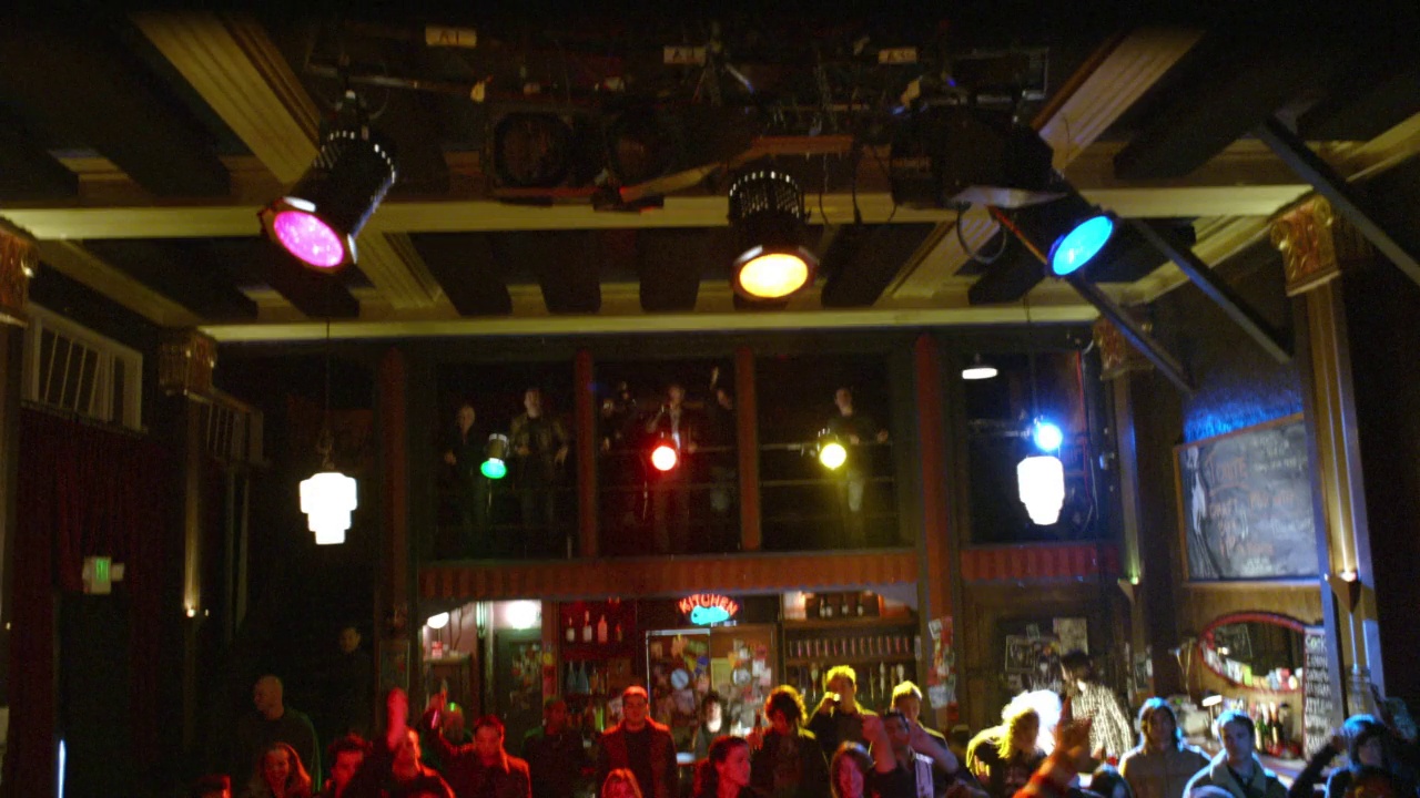 从左到右的夜总会观众和摇滚乐队或朋克乐队表演的舞台。观众们，一群男男女女随着音乐跳舞。观众聚集的房间后面的二层阳台。歌手吉他手都是长头发的男人。METALH视频素材