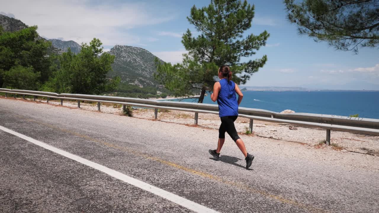 年轻活泼的运动型女子沿着布满岩石的海岸在路上奔跑。户外跑步练习。积极的胖乎乎的女性做有氧运动，试图减肥。慢跑的概念视频素材