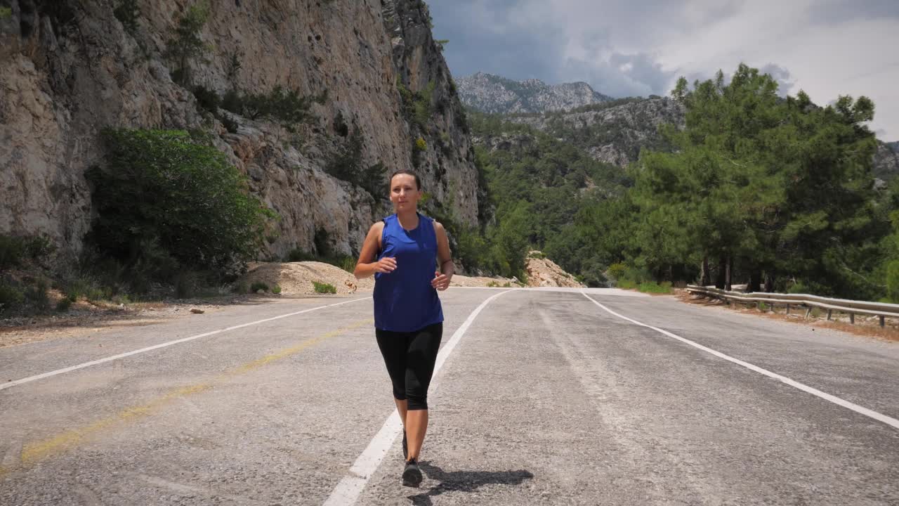 女人户外训练。活跃精力充沛的女性在空旷的山路上慢跑，做健身运动，有氧锻炼。在山区训练耐力跑的体育运动员。运动动机视频素材