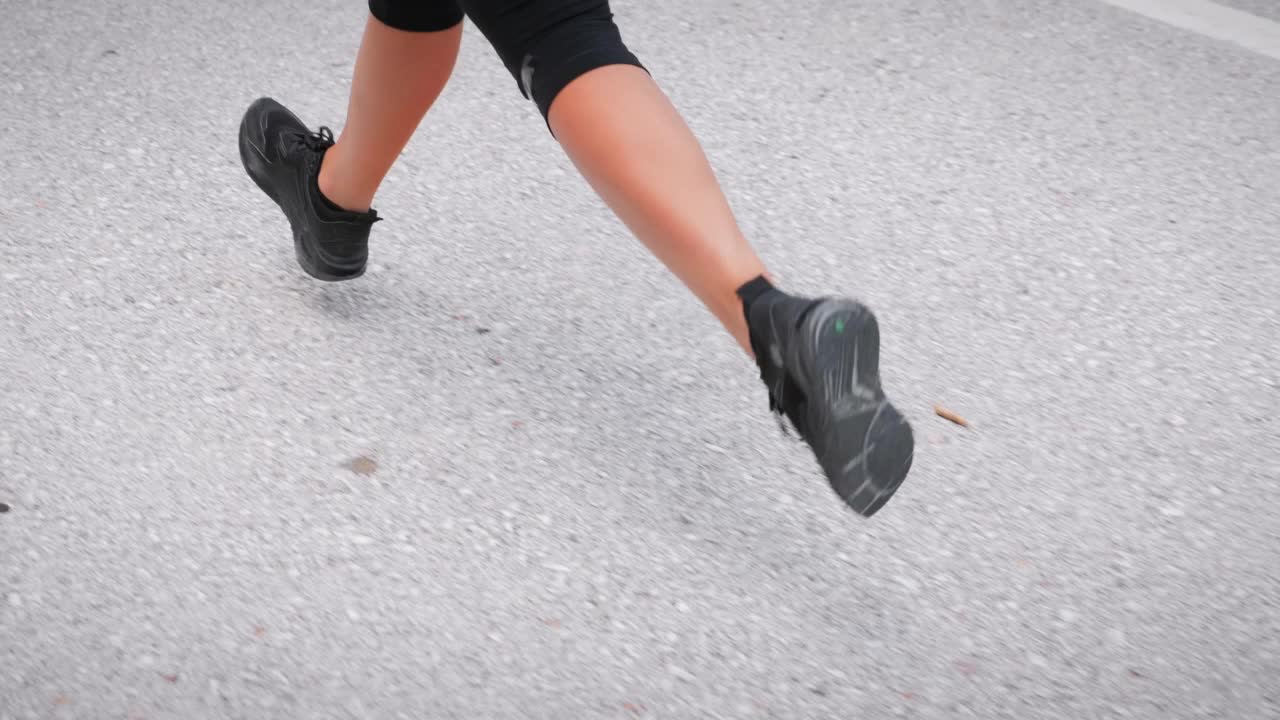 穿着黑色运动鞋的女性双腿在空荡荡的柏油路上奔跑。喜欢运动的女人，脚上肌肉发达，早上慢跑，做剧烈的有氧运动。健身娱乐活动视频素材