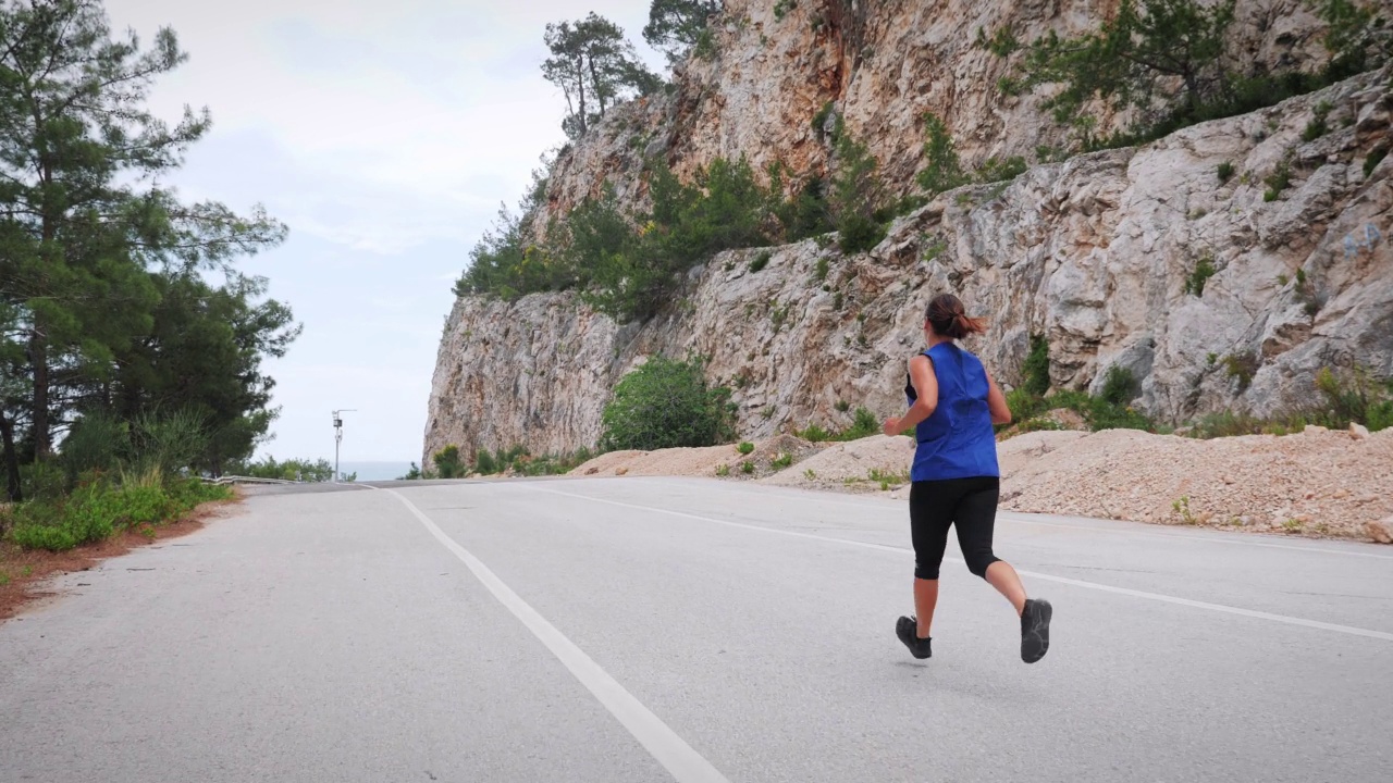 女人在路上跑得很快。活跃的运动型女性在阳光明媚的夏天沿着岩石悬崖慢跑。健身运动的动机。有氧运动激烈的运动。娱乐休闲活动视频素材