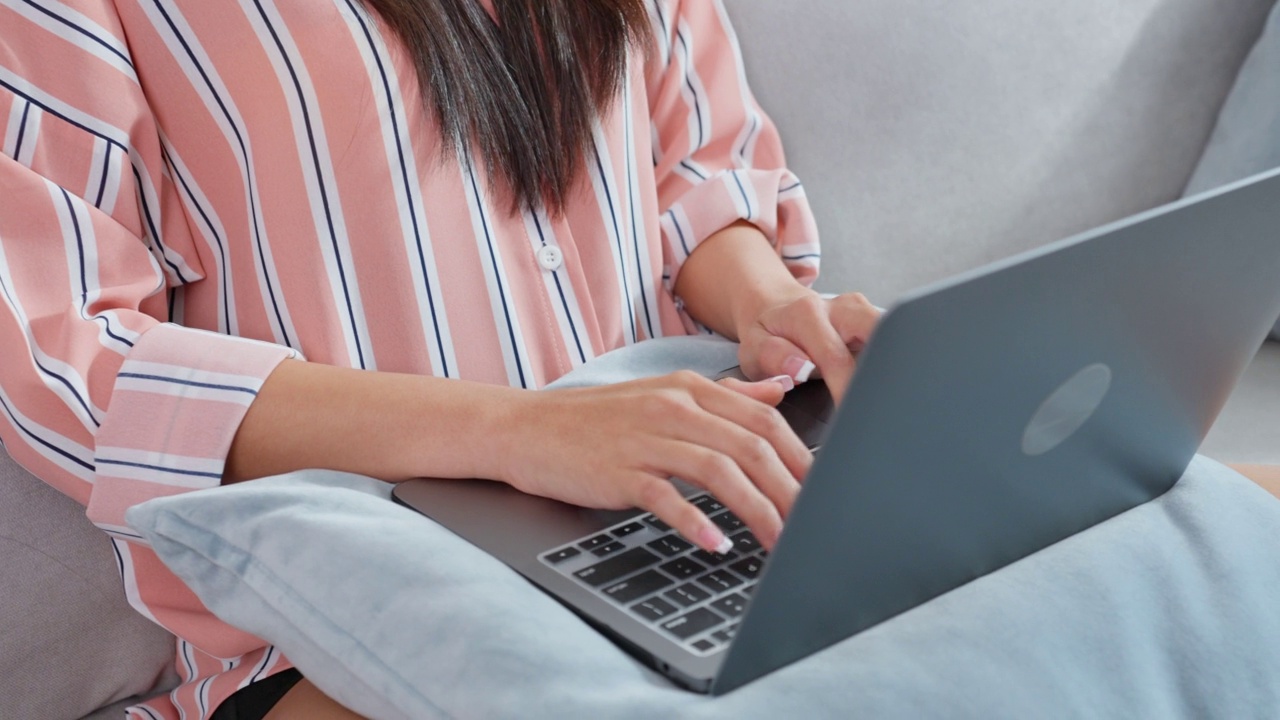 亚洲年轻女商人在电脑上打字，在家工作。漂亮迷人的自由职业女职工坐在沙发上，用笔记本电脑在客厅的幸福和微笑的房子视频素材