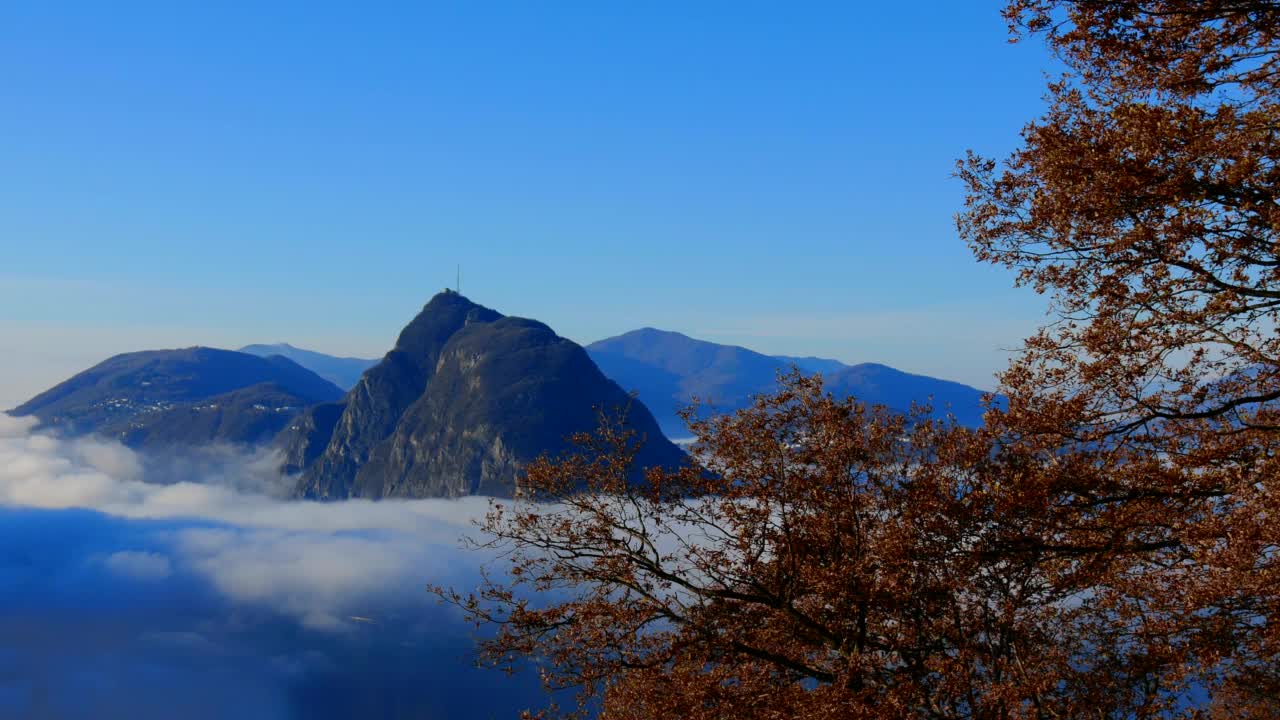 高山湖卢加诺的全景与云海、山和树在晴朗的秋日视频素材