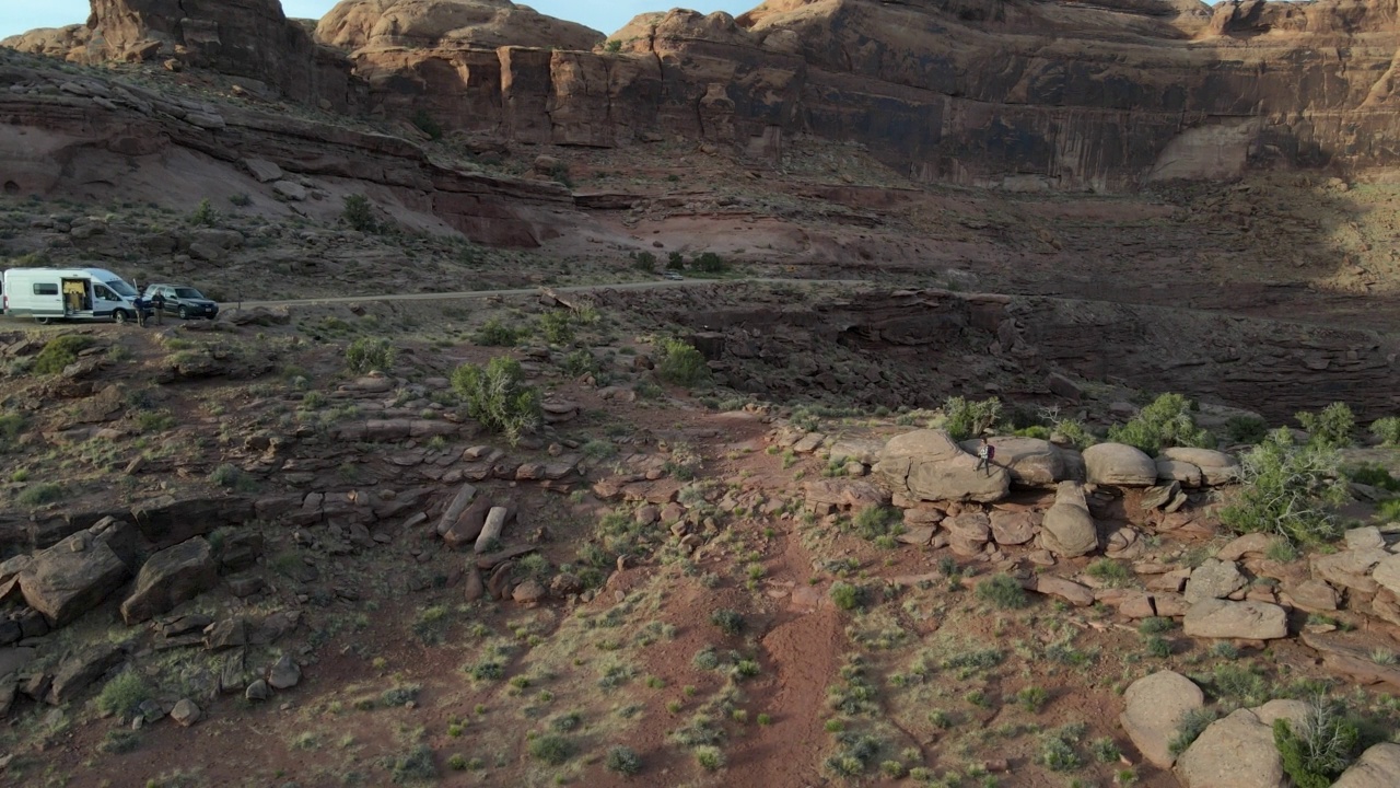 无人机漂亮的运动年轻女子徒步在广阔的沙漠景观摩押在犹他州西南沙漠与露营车视频素材