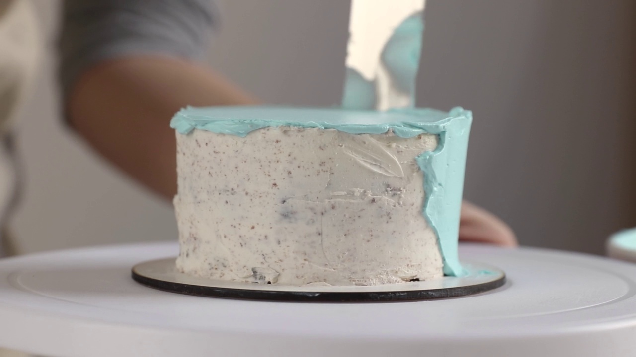 糖果商在圆形蛋糕的一侧用烹饪抹刀近距离抹上蓝色奶油视频下载