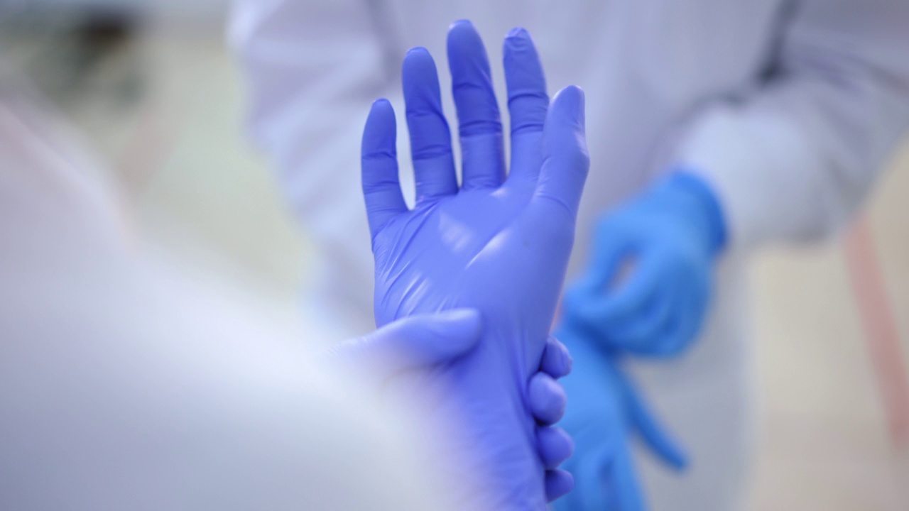 特写两个不知名的女医生戴上橡胶手套。在医院室内准备外科手术或体检的白人妇女。视频素材