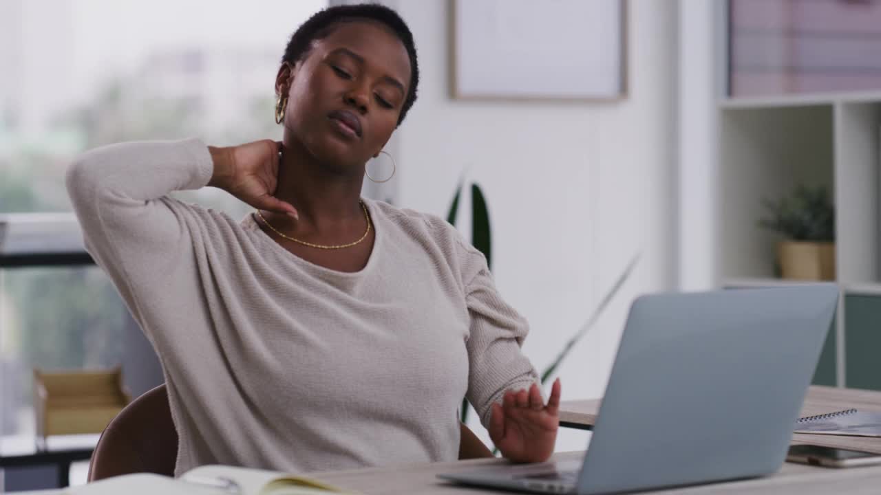 20多岁的年轻非洲裔美国女商人在现代办公室的办公桌前休息时因颈部疼痛而使用笔记本电脑。一名非洲裔美国女商人因颈部疼痛而使用笔记本电脑，并在工作时在办公桌前打盹。视频素材