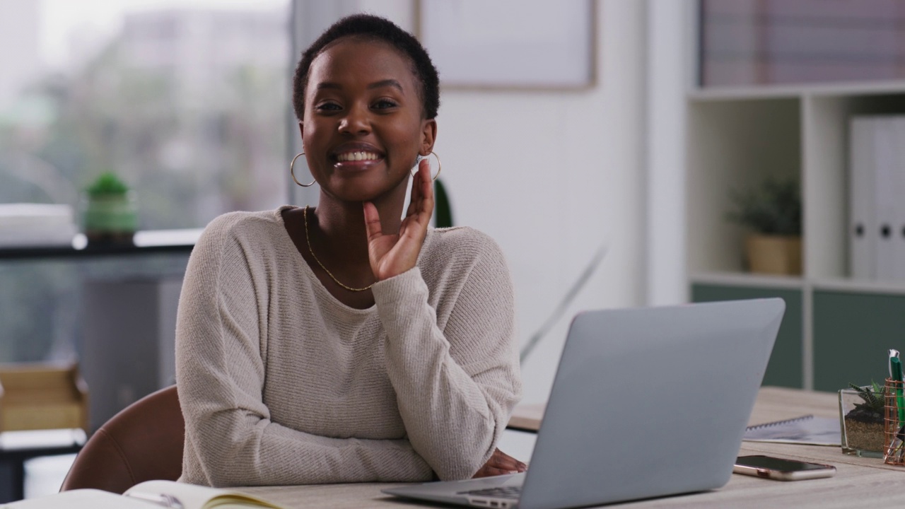 非裔美国女商人独自坐在办公室用笔记本电脑坐在办公桌前工作。一位非裔美国女商人微笑着，看起来很自信，同时使用笔记本电脑，在一个现代化的办公室工作。视频素材