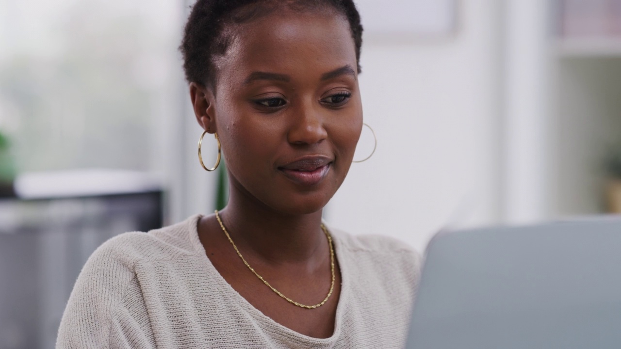 一名非裔美国女商人在办公室工作时使用笔记本电脑，看起来很开心和微笑。快乐的女商人在办公室里用笔记本电脑工作。视频素材
