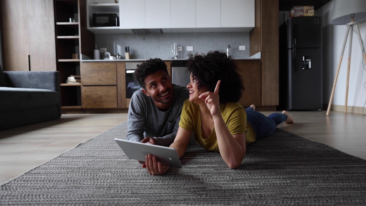 幸福的夫妇躺在地毯上，用平板电脑上的应用程序思考着房子的装饰视频素材