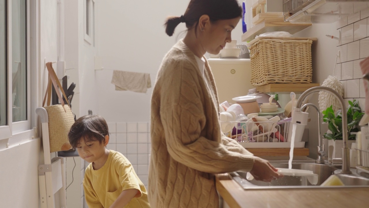 亚洲美女妈妈教小男孩打扫厨房。视频素材