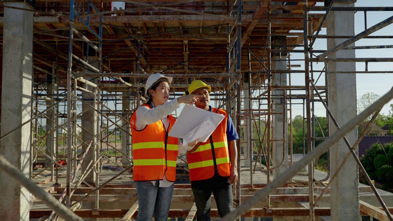 年轻的亚洲女工程师和工头拿着蓝图在施工现场检查施工是否按计划进行。视频素材