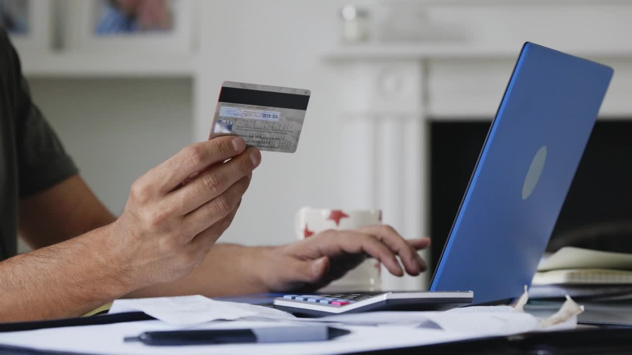 一个用笔记本电脑用信用卡在网上支付账单的人视频素材