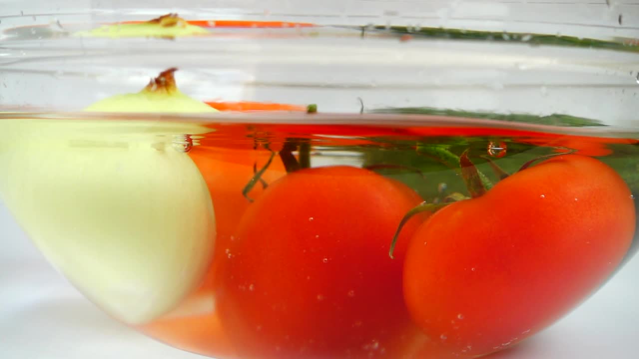 西红柿、洋葱、黄瓜和红灯笼椒放在盛水的玻璃碗里。缓慢的运动。视频下载