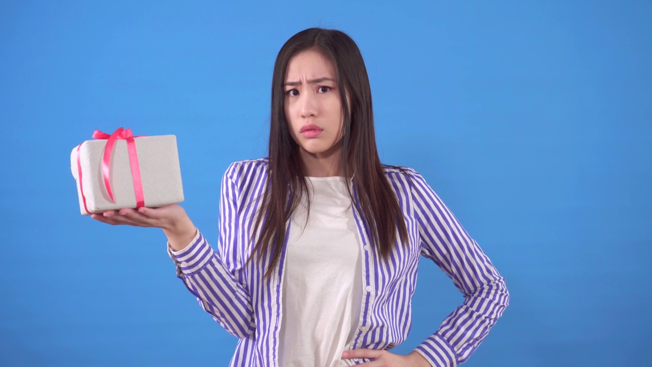 不满的年轻亚洲妇女与一个小礼物在蓝色的背景视频下载