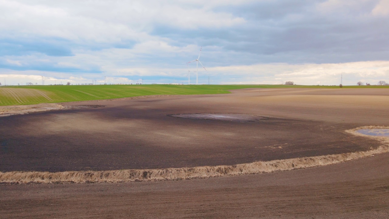 耕地肥沃的土壤附近的干燥池塘和风力涡轮机农场的背景视频素材